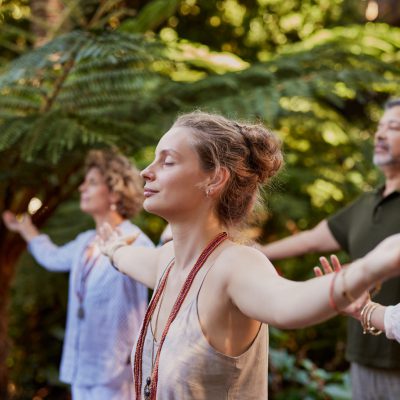 A diverse group practicing mindful breathing with arms outstretched in a peaceful forest setting. Muliethnic people meditating outdoors with eyes closed, focusing on healing and connection. Participants enjoying a wellness retreat surrounded by nature, practicing gratitude and holistic exercises .